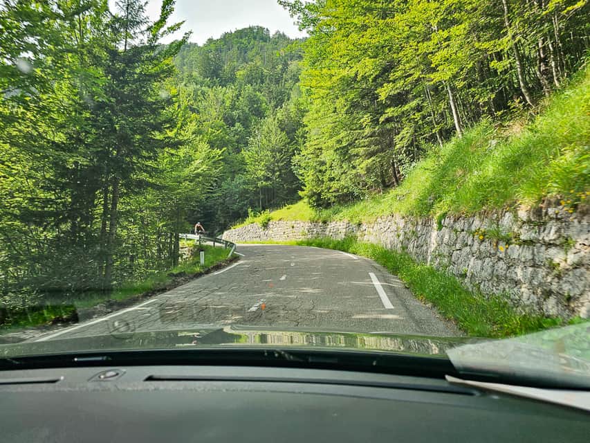 A mountain road with stone wall on one side with trees beside the road.