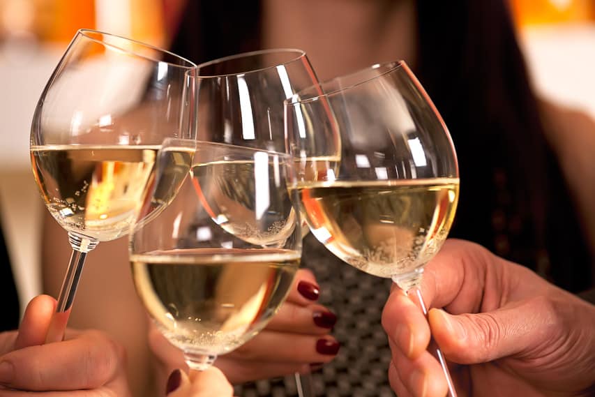 4 glasses of white wine with wine swirling around with lights in the background.
