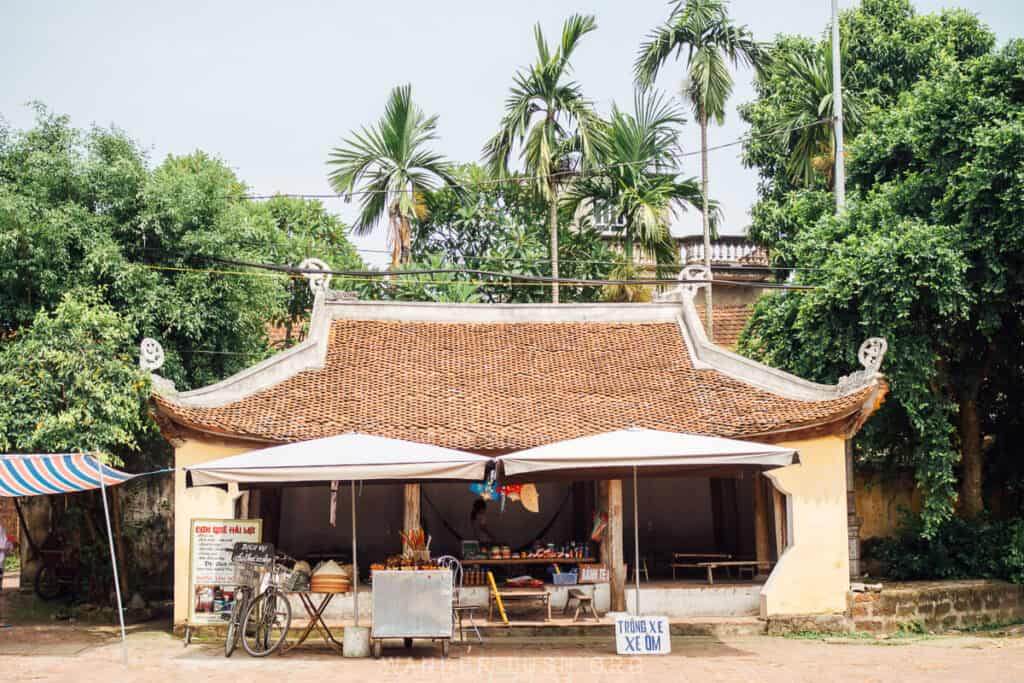 A small street cafe with an arched roof with bamboo shingling and umbrellas outside.