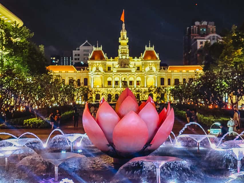 A lit up flower fountain and lit up gold building.