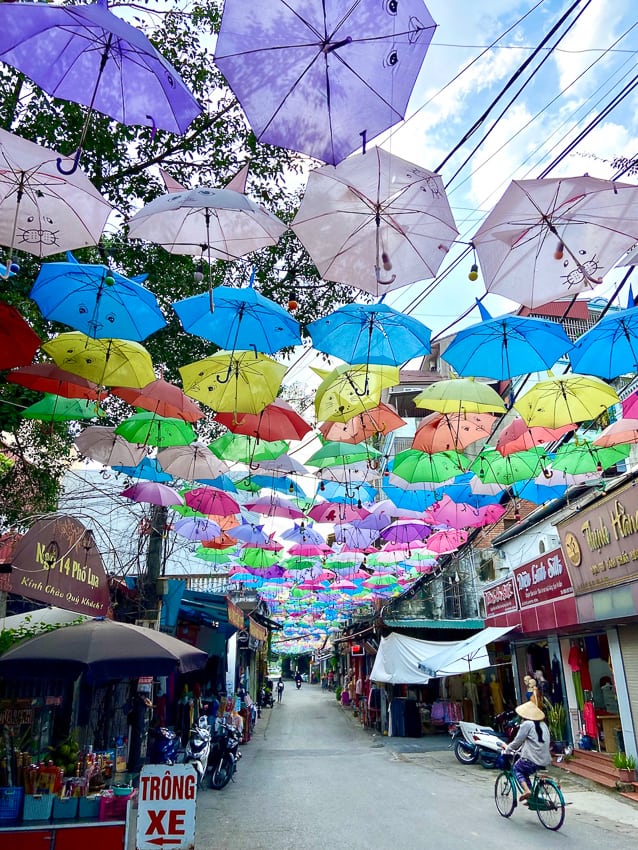 People walk through a market alley with a roof of colorful rows of umbrellas.