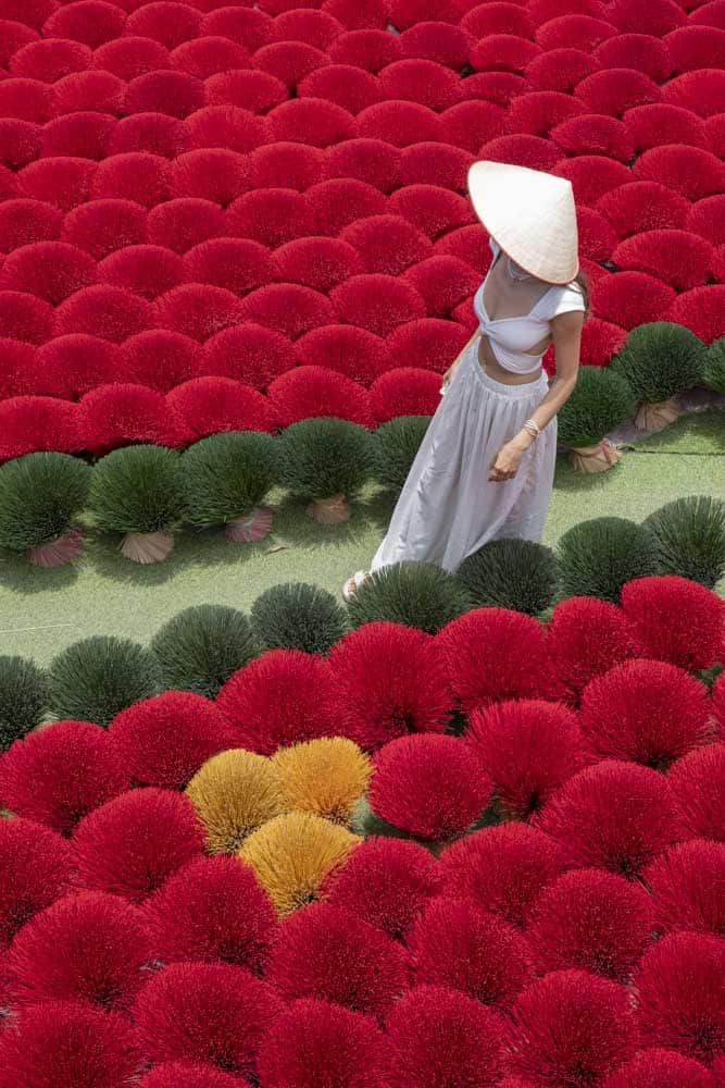 A woman strolls through a field of colorful bundles of incense.