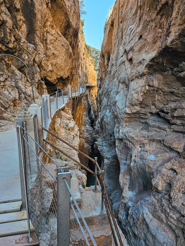 A rock cement path leads across the edge of the rock down into a dark rock cavern.