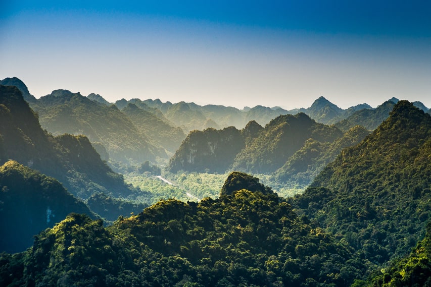 The landscape of the overlapping hills with trees covering the entire surface of the hills. There is a small fog covering the base of the rocks.