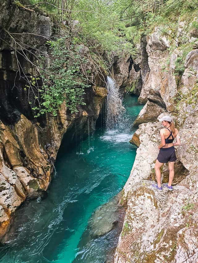 A woman stands on a rocke dge looking at water spewing off into the Soca river.