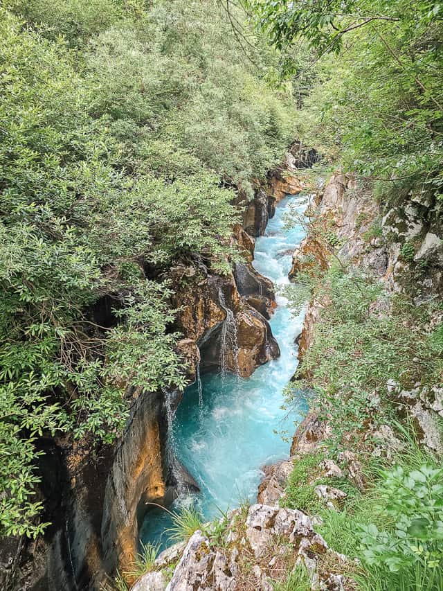 Water crashes down rocks into a blue water Soca River in a rock gorge.