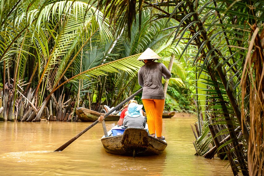 A tour guide rows people through the bamboo and mud river.