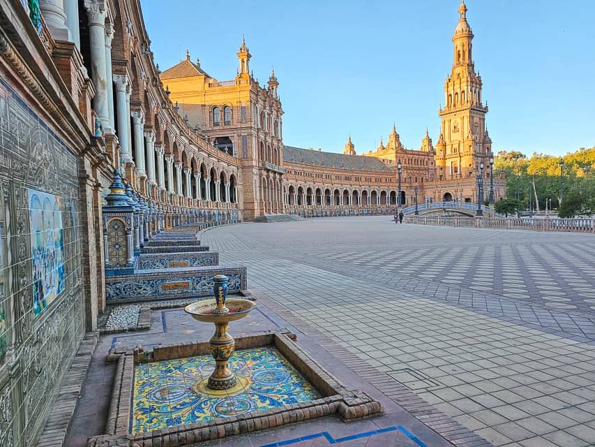 A beautiful spanish courtyard with the sun just peeking out in the colorful tile courtyard with pillars holding up a castle-like stone building.