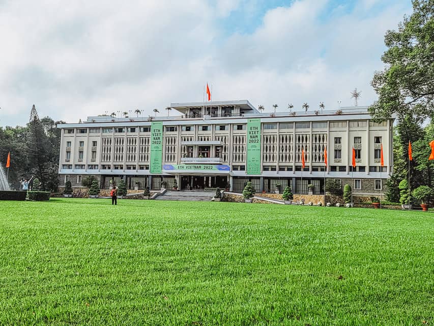 A large, wide cream colored building with orange flags circling the area and oval windows carved into the exterior.