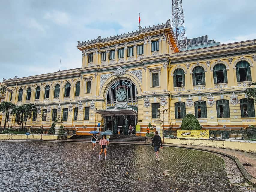A grand yellow post office with a large clock and tile street.