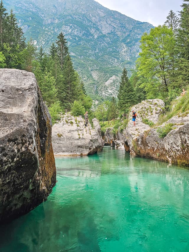 People stand on the huge rock looking at the mouth of the blue water river.
