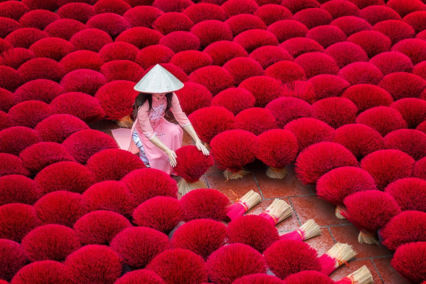 An asian woman in a pink dress working on red bundles of incense.