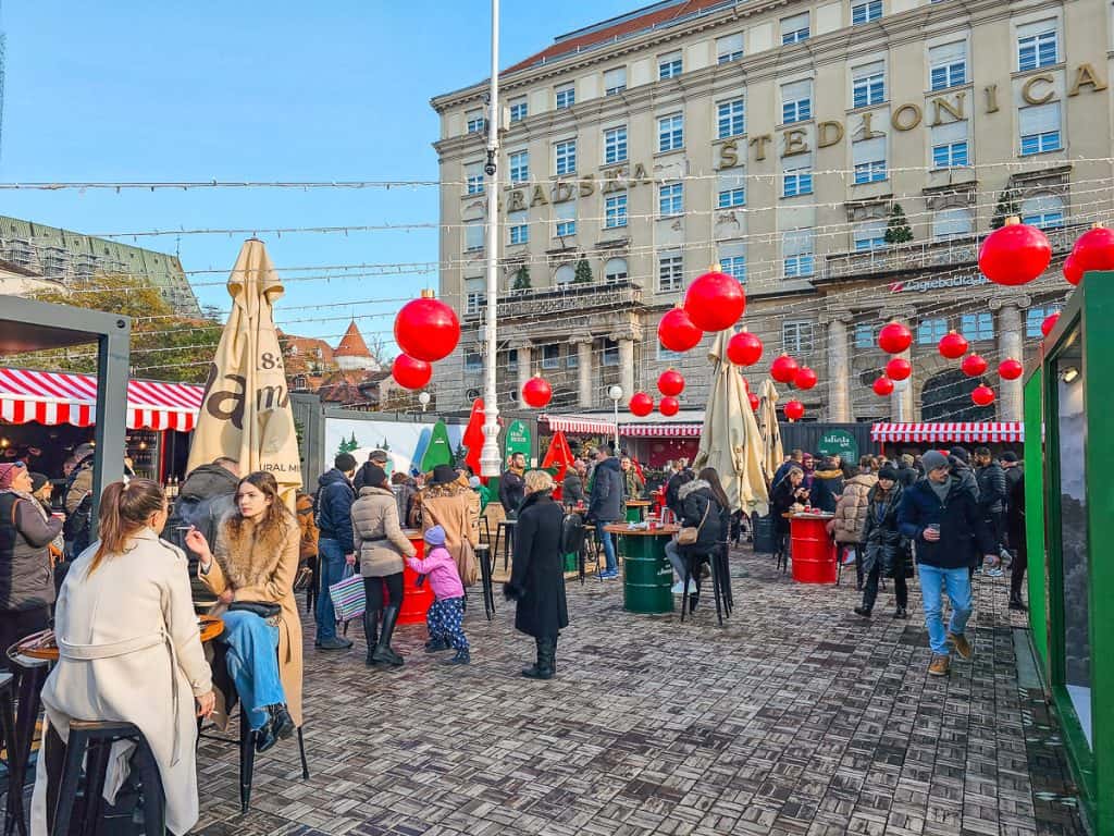 Lots of people walk around a decorated spot of the market with lights and red balls over the top of the stalls.