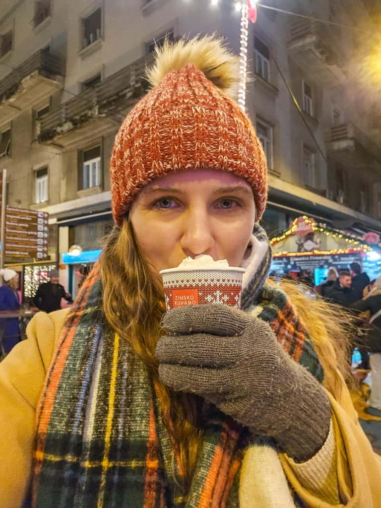 A woman in a red hat holds a red and brown cup that has whipped cream piled up on top.