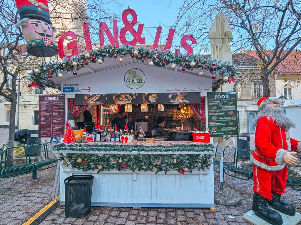 A small white wooden stall decorated with garlands and ornaments selling assorted food and drinks.