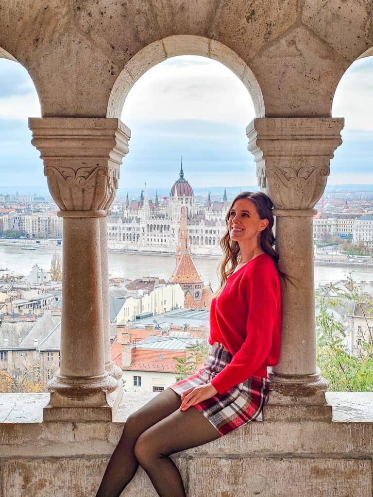 A woman sits on the edge of the Fisherman's Bastion looking out at Budapest.