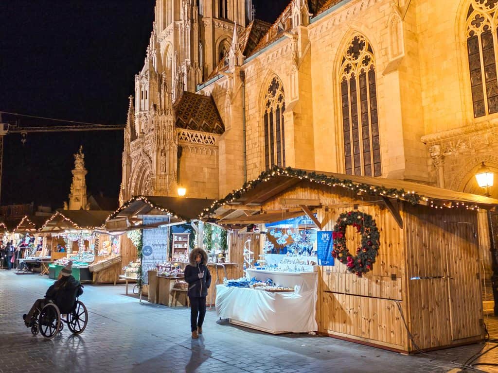 Some bamboo stalls with lights are lined up in front of a cathedral selling souvenirs and hot chocolate.