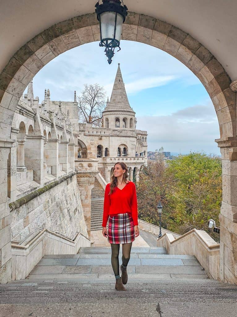 A woman with a red sweater and red and black plaid skirt walk on the steps along the castle towers.