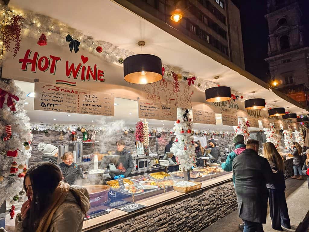 A drink and food booth with lots of twinkle lights and small white trees.