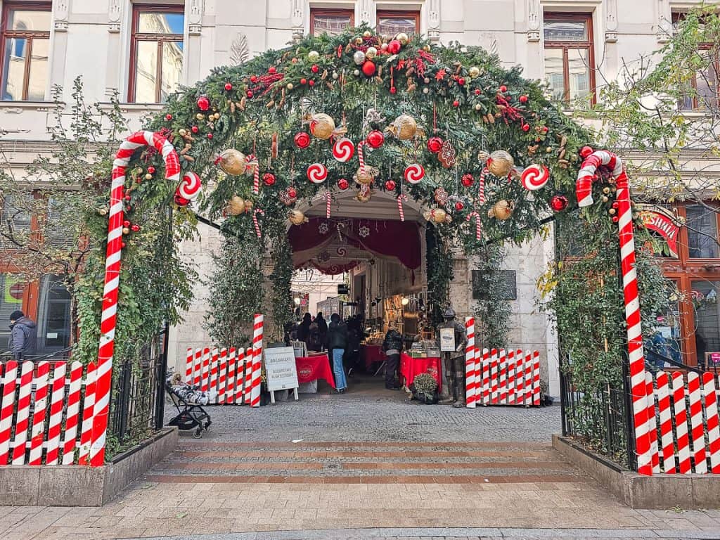 An arched way completely covered in decorated garlands with candy cane fences right next to it.