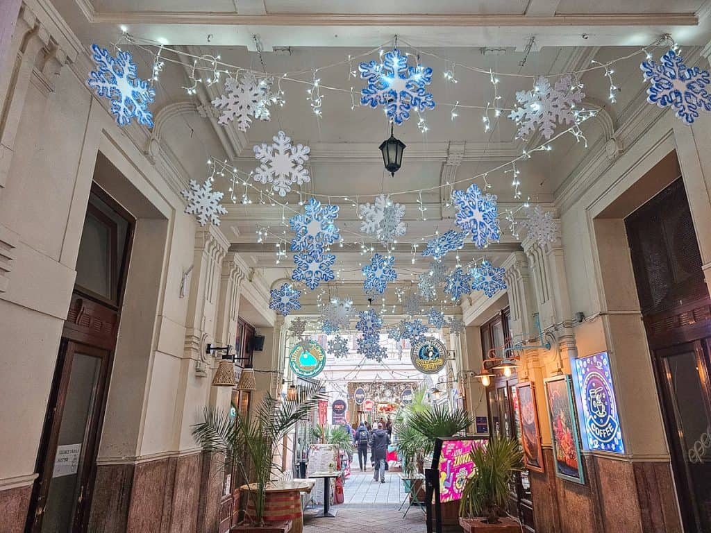 An alley with wooden doors and lit up snowflakes strung from the ceiling going down the alley.