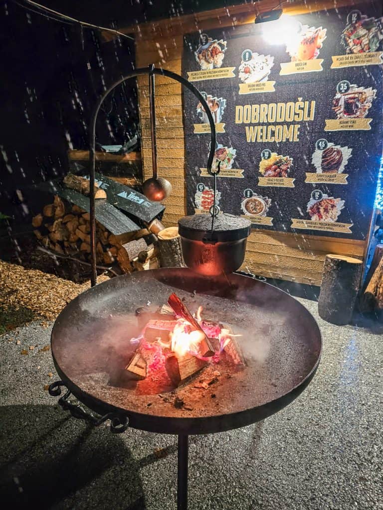 A metal fire ring in front of a wooden stall with a small orange and red fire burning inside of it.