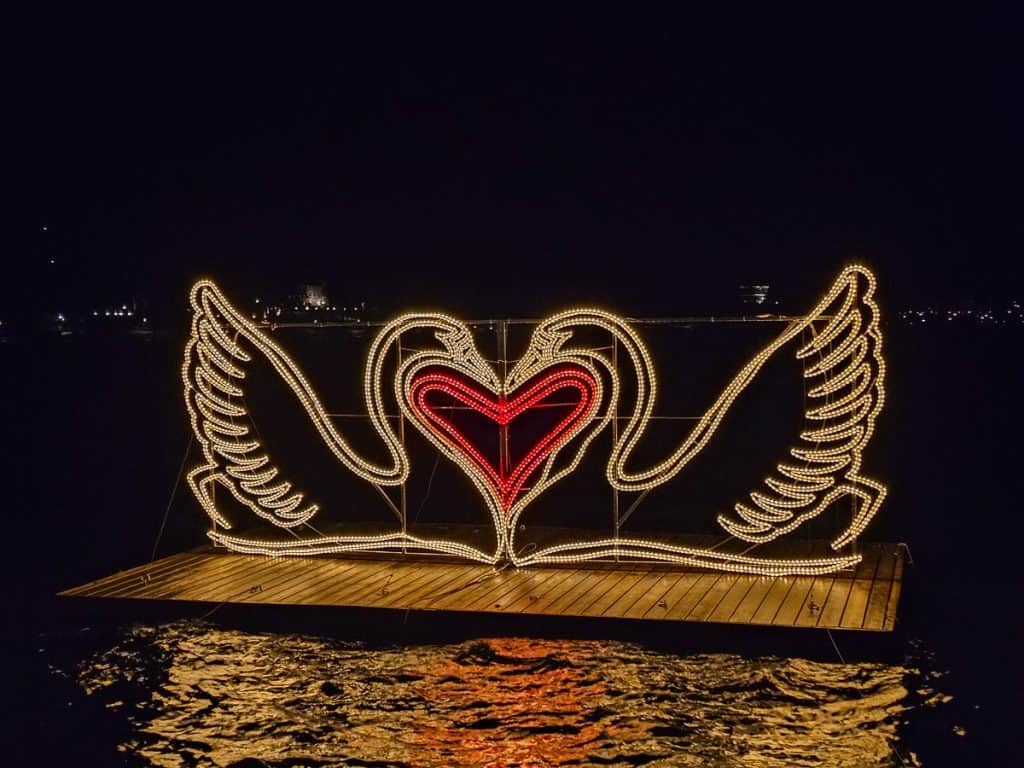 A light exhibit (that shows two swans kissing with a heart between them) that is floating on the lake.