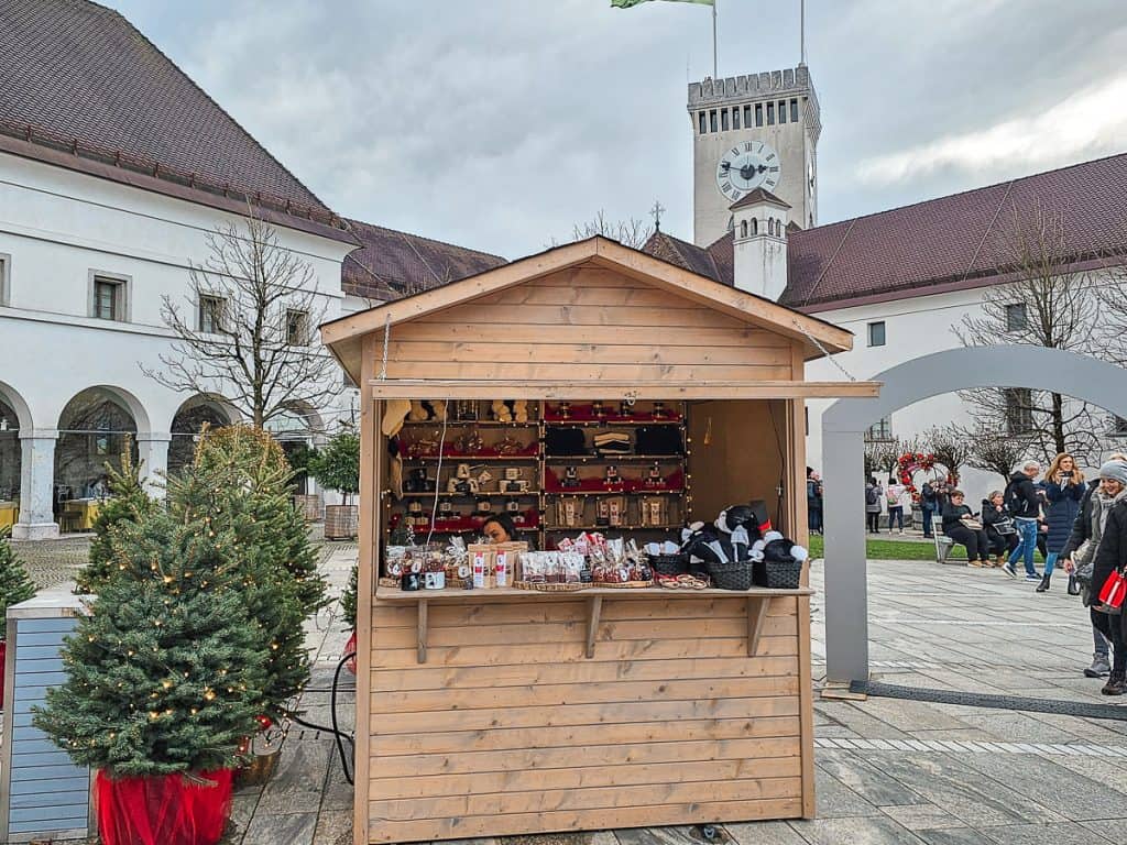 A small wood hut selling cookies and souvenirs at the town square with 2 Christmas trees on the side.