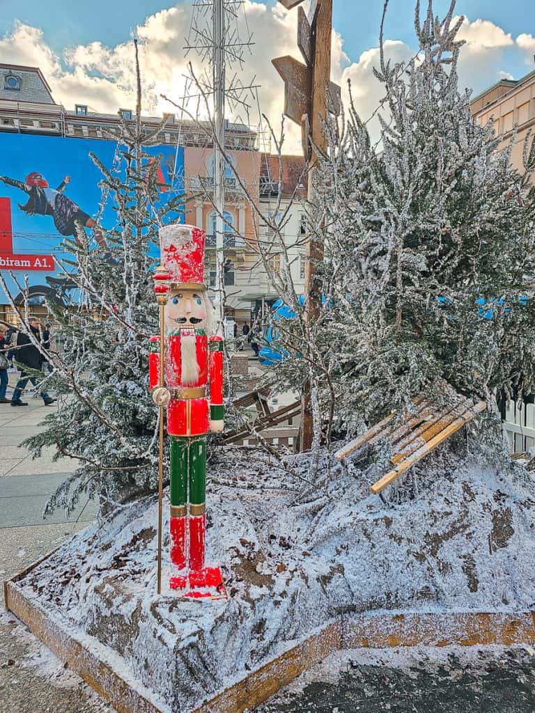 A small red nutcracker sits on the edge of a white snow covered tree