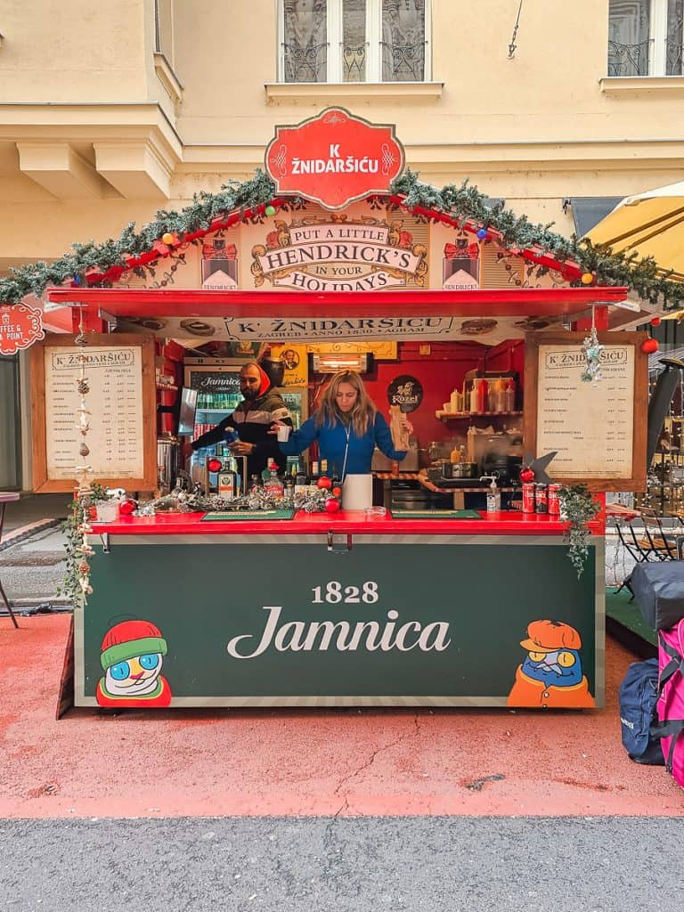 A red and green drink stand that is decorated with garlands and is lit up with Christmas lights.
