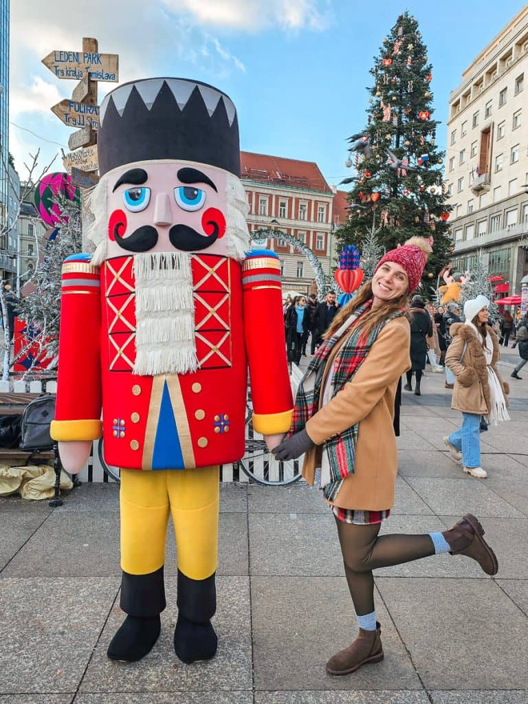 A woman holds a 10-foot nutcrackers hand that is painted with a red suit and yellow pants.