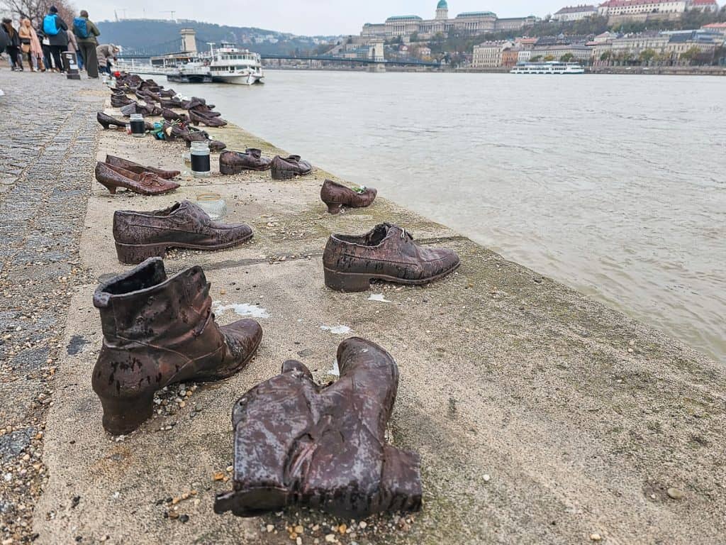 A sandy coast line with lots of dirty and worn out shoes on the edge of water.