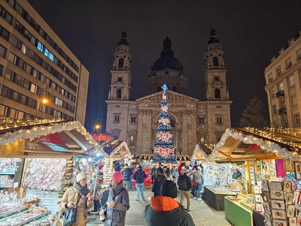 The St. Stephen's Basilica Market with lots of wooden stalls selling pictures and souvenirs with a huge Christmas tree with the stone church in the background,