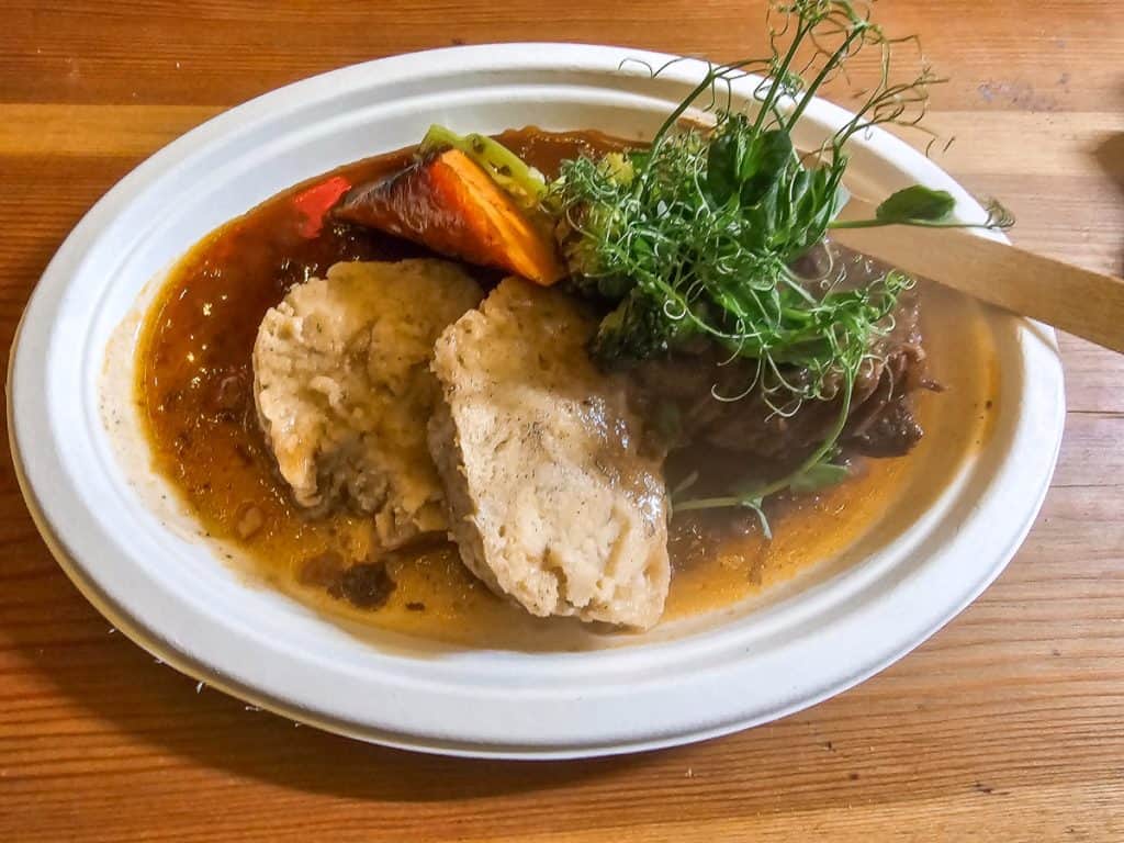 Tender pieces of white meat with dark orange carrots and kale sitting in a stew of broth on a white paper plate on a white table.