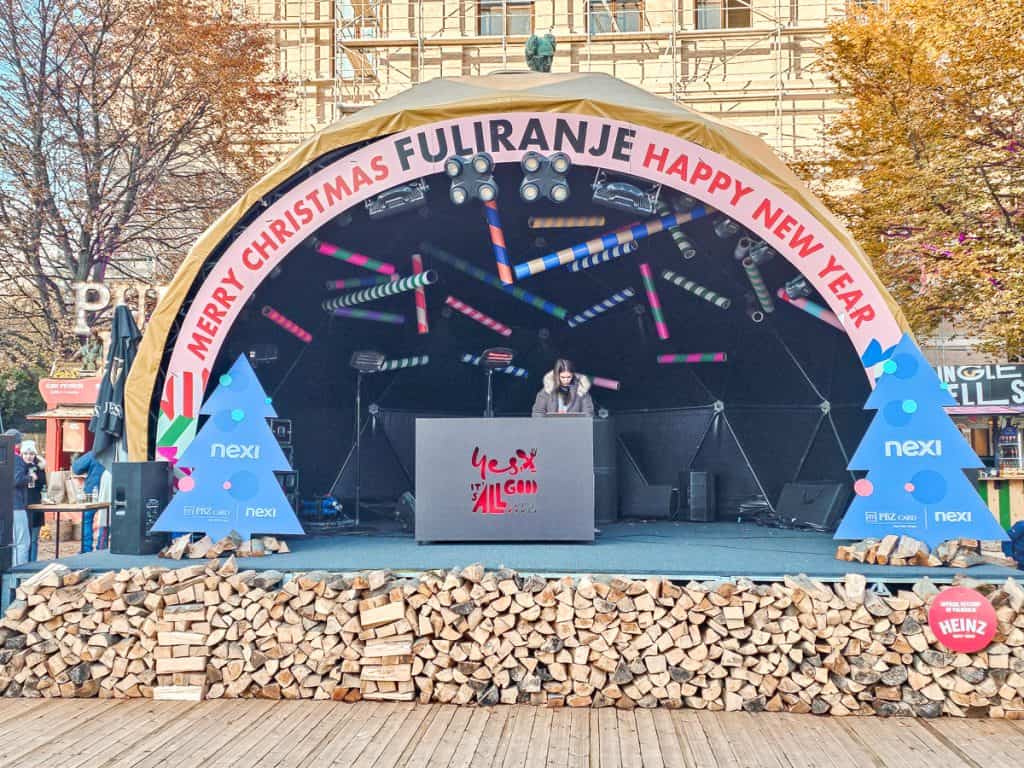 A stage with blue Christmas trees on the side and an arched roof. The stage is stacked up on hundreds of pieces of wood.