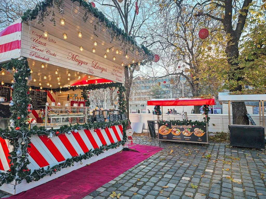 A wooden stall and booths with candy cane stripes on the exterior and garland with lights trimming the edges.