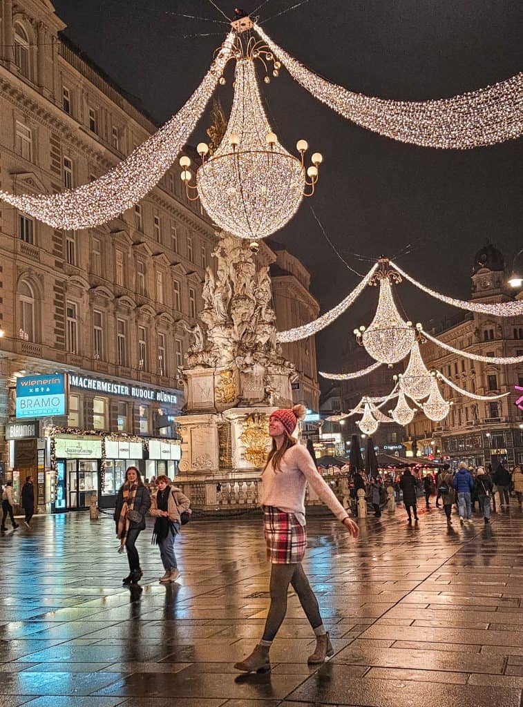 A woman walks in the square with chandilers and lights strung across 
the buildings 
