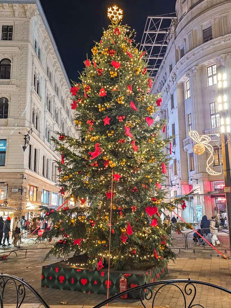 A large Christmas tree with gold beaded chains and red shaped ornaments.