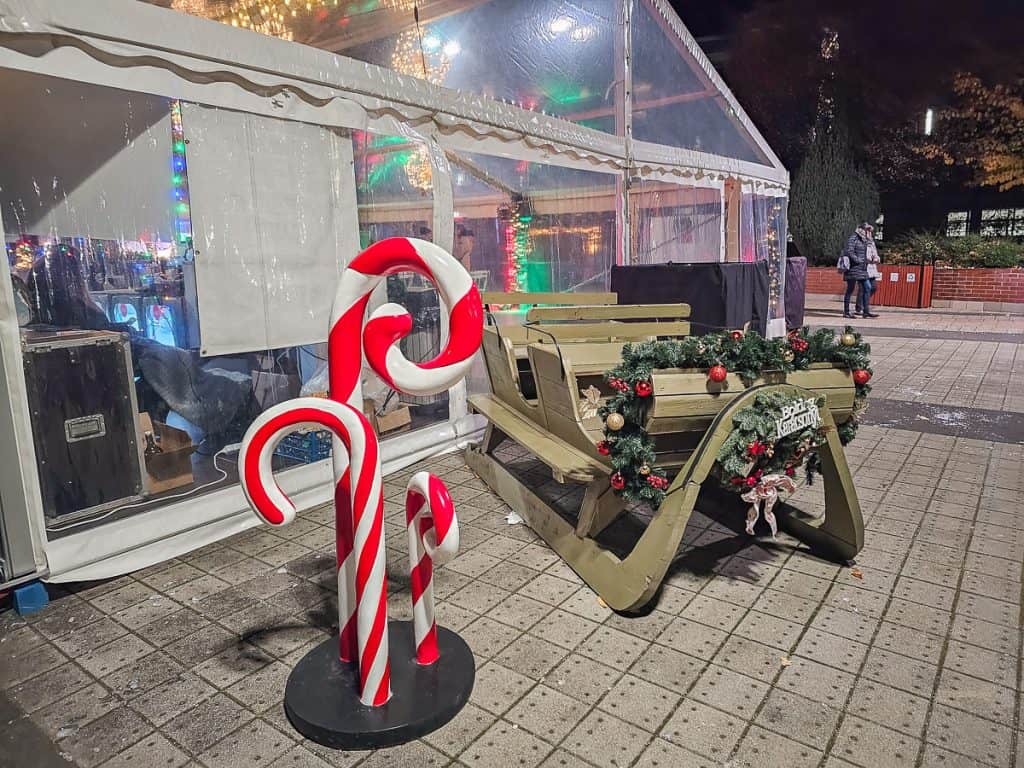 The outside of a restaurant with a sled for people to sit on and a decoration of 3 large candy canes right next to it.